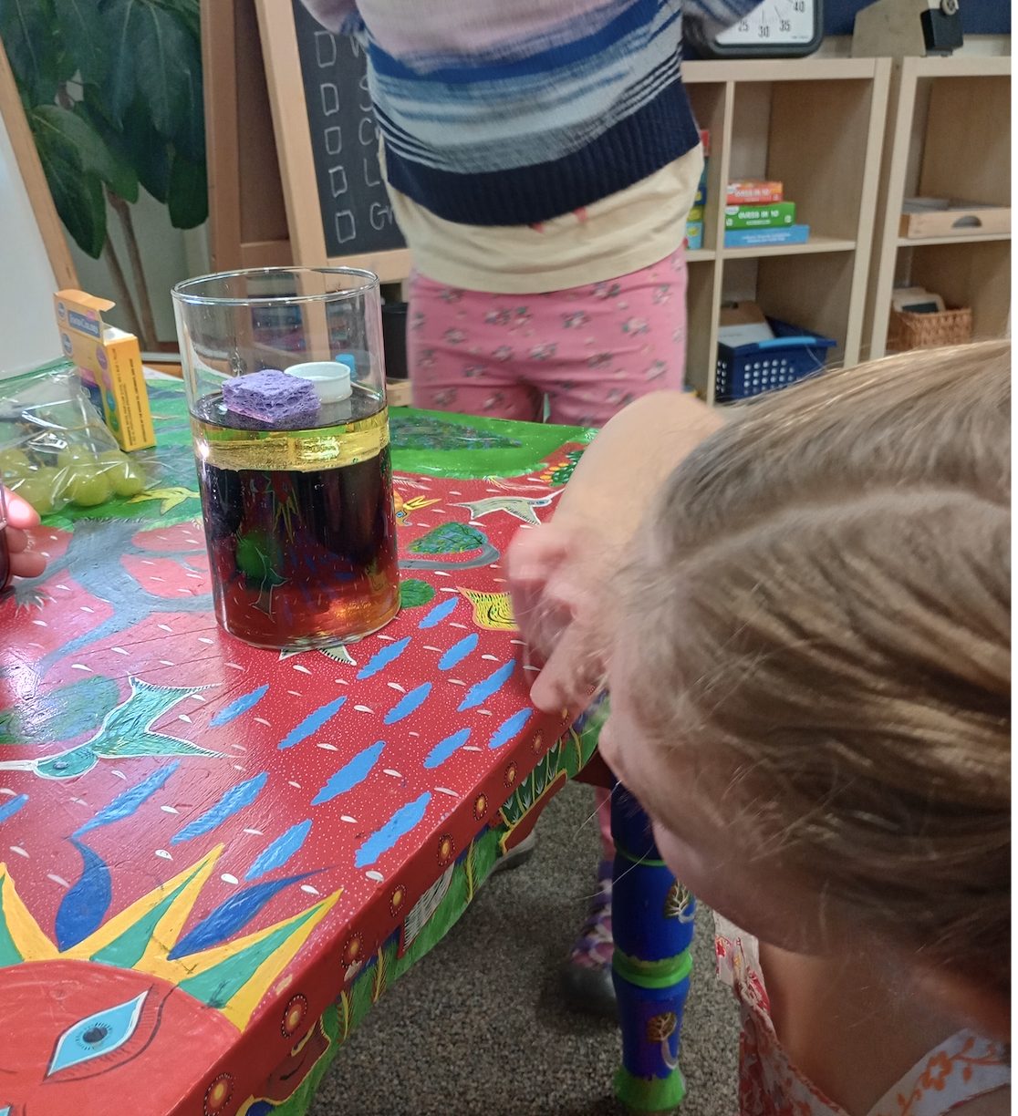 A child watches a colorful oil-and-water science experiment in a glass jar