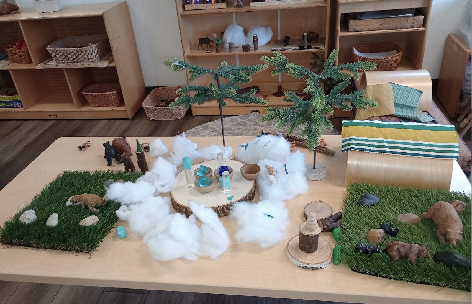 A small-world play setup at Bixby Academy with toy bears, fake snow, pine trees, and grass mats arranged on a table