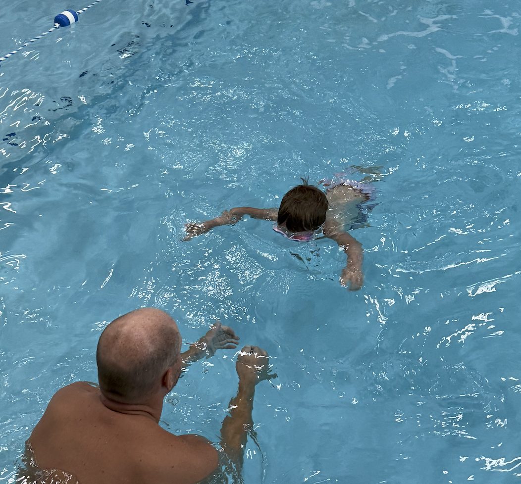 A child swimming in an indoor pool with an instructor coaching from the side